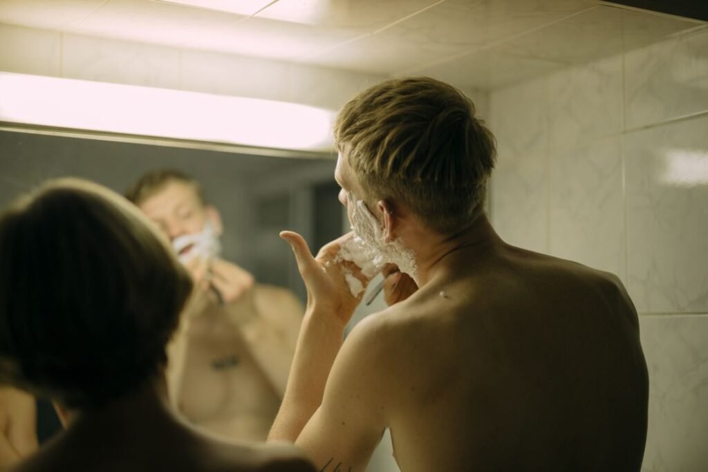 Man shaving his beard in front of a bathroom mirror