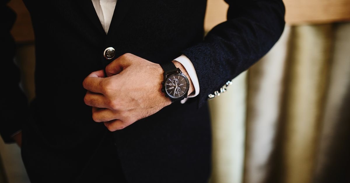 Man in a dark suit wearing a menswear accessory dress watch while adjusting his blazer lapel